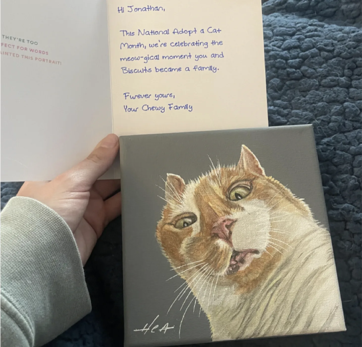 A customer holding a hand-painted cat portrait beside the handwritten Chewy card it arrived with